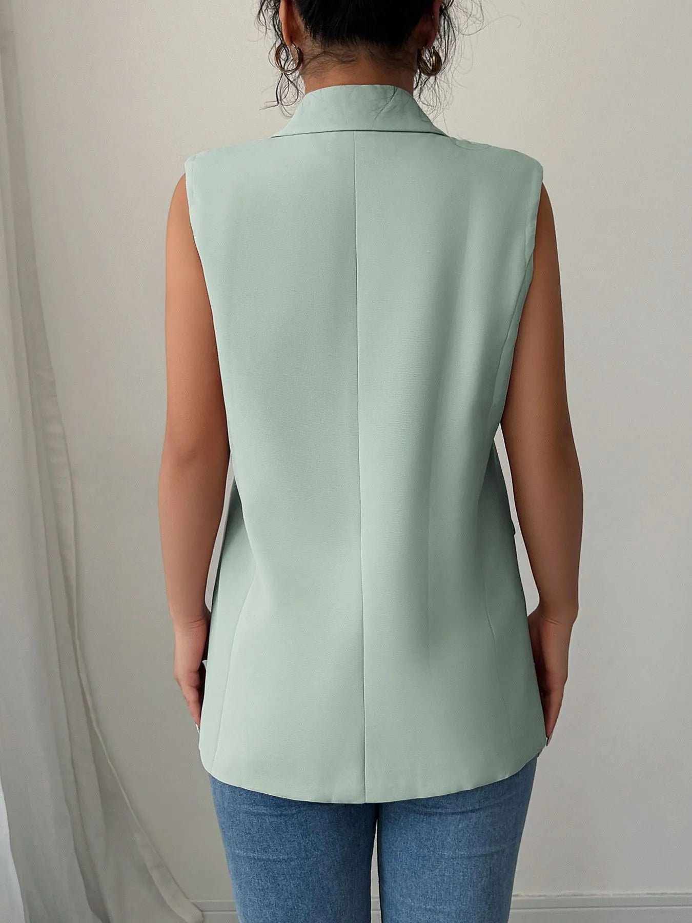 Back view of a model wearing the One Button Sleeveless Blazer in mint green, paired with denim jeans.